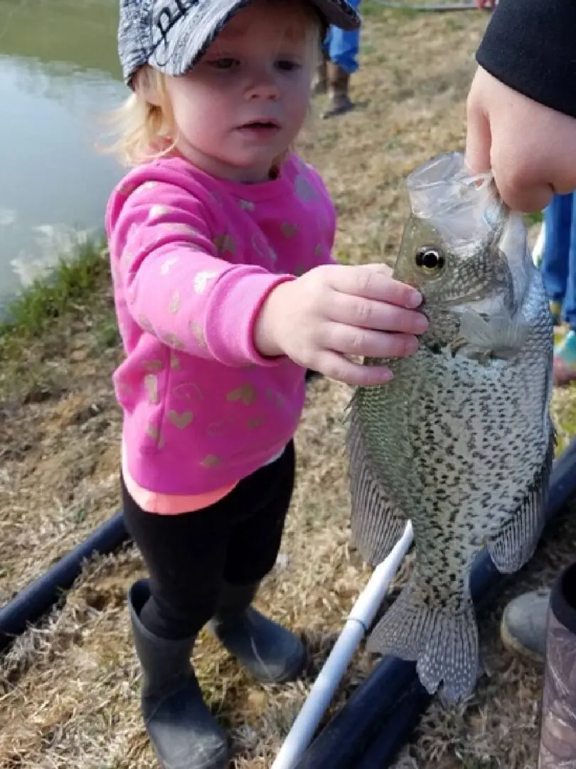 A little girl holding onto a fish while standing next to another child.